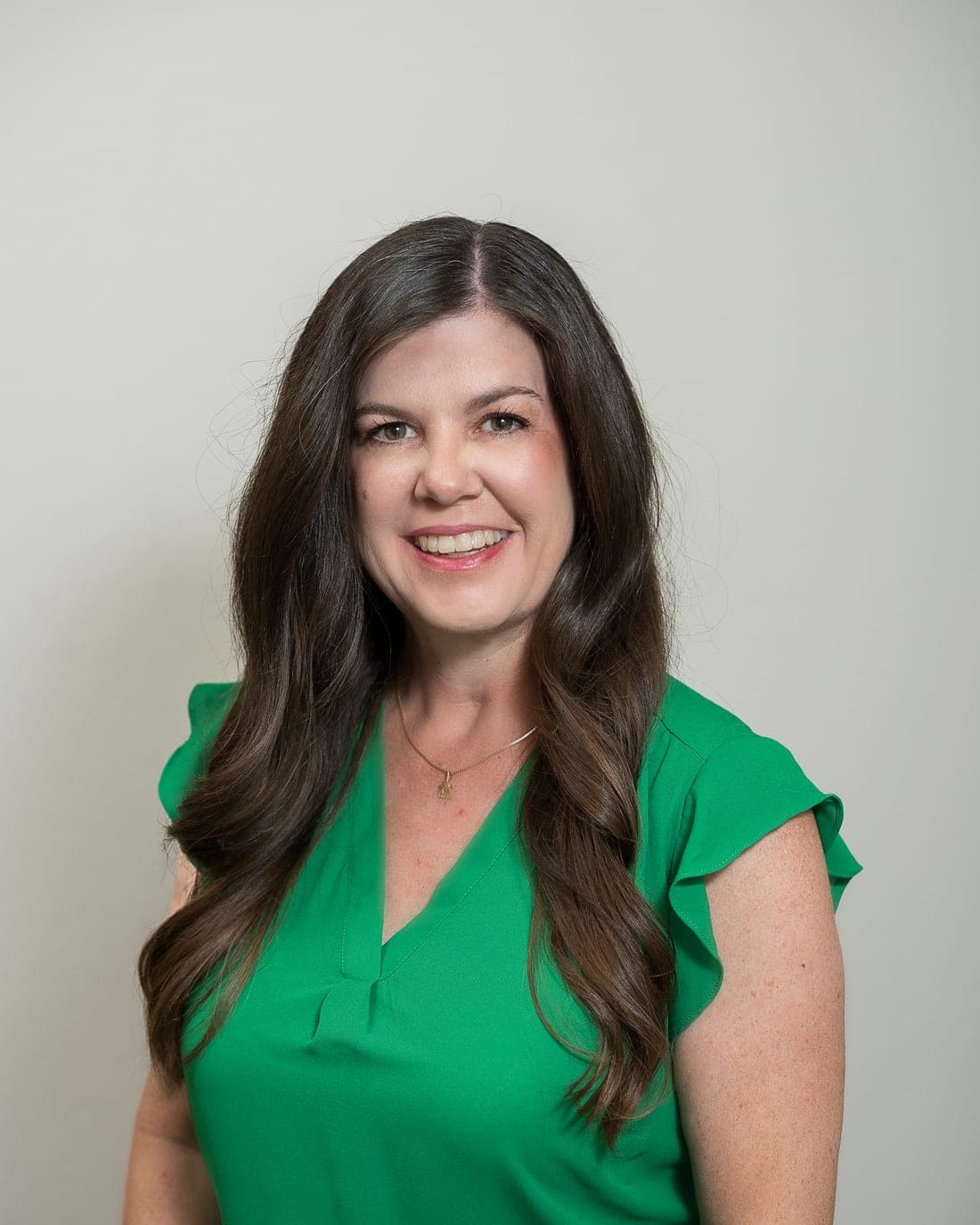 Rebecca Gassett, smiling, in a green blouse against a plain warm background.