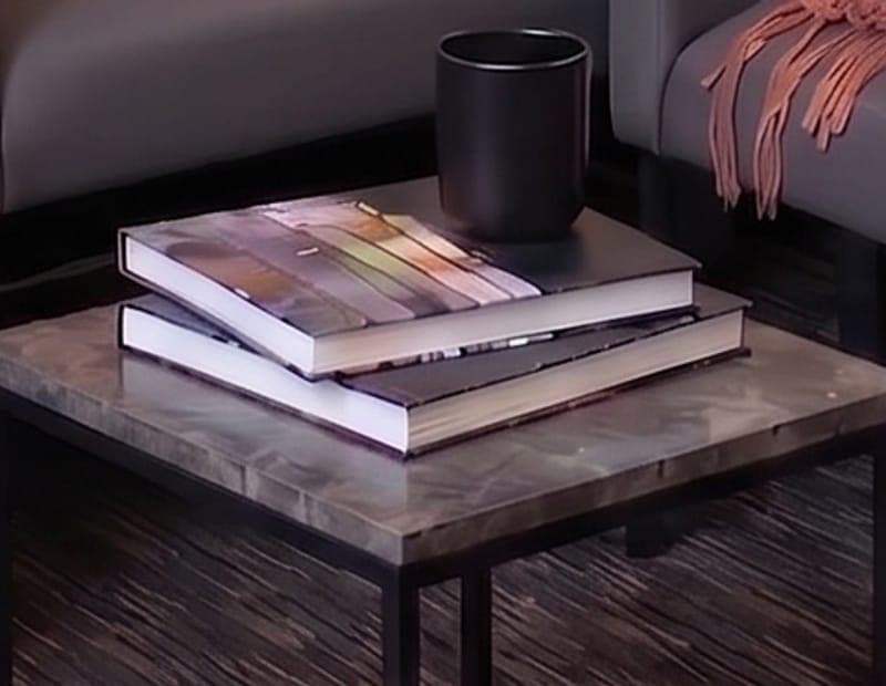 Two hardback books stacked beside a black mug on a marble side table.