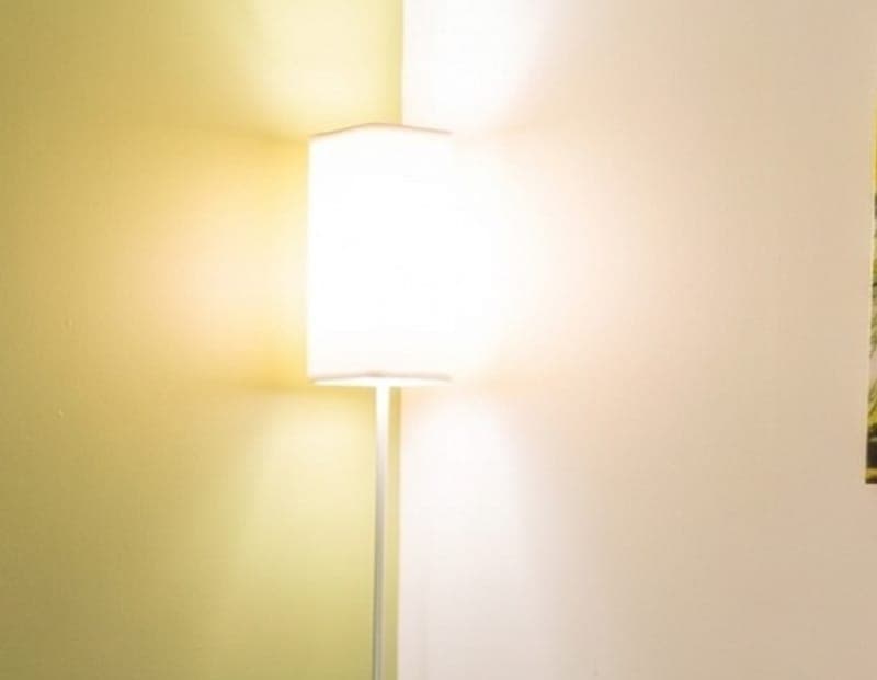 A floor lamp glowing warm against an olive green wall.