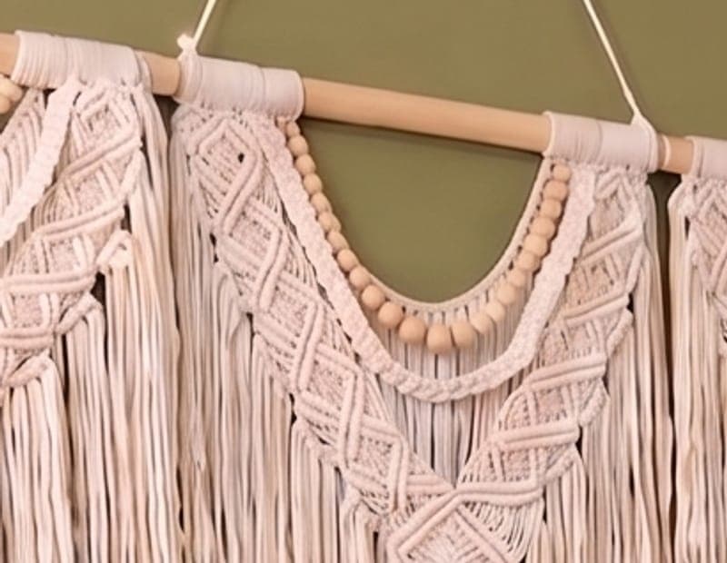 A close view of knotted cream cord and wooden beads on a macramé panel.