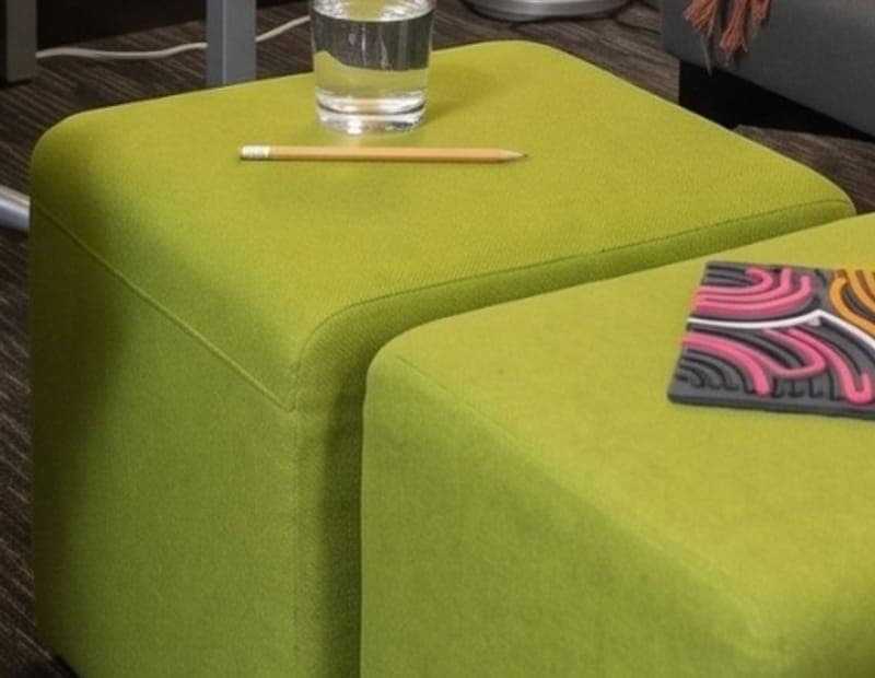 Two lime green ottomans with a glass of water and a pencil resting on top.