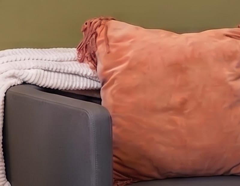 A chunky white ribbed throw draped over the arm of a gray chair beside a terracotta cushion.