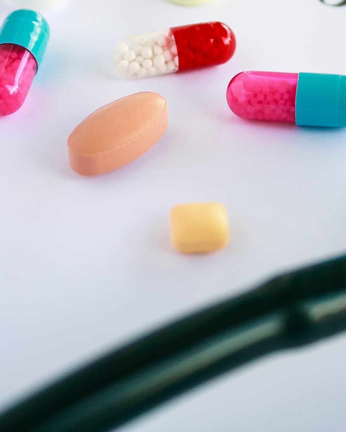 A few colored tablets and capsules on a white desk beside a stethoscope.